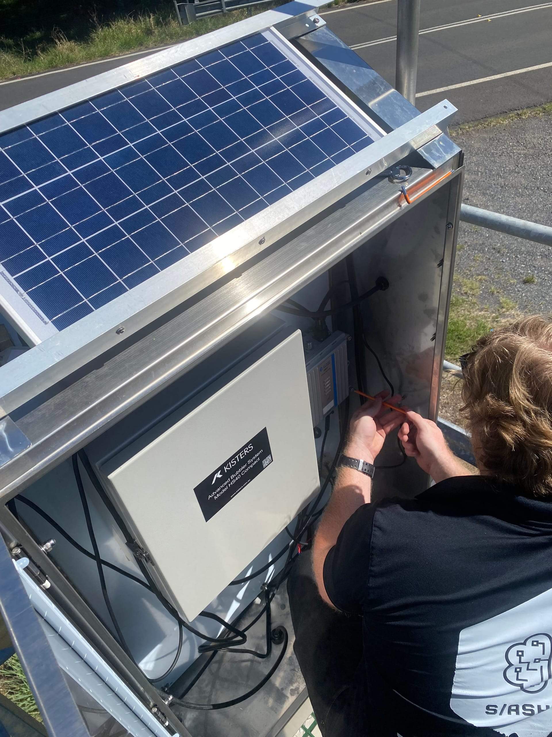 A SlashTech technician wiring a solar-powered monitoring enclosure on an access platform